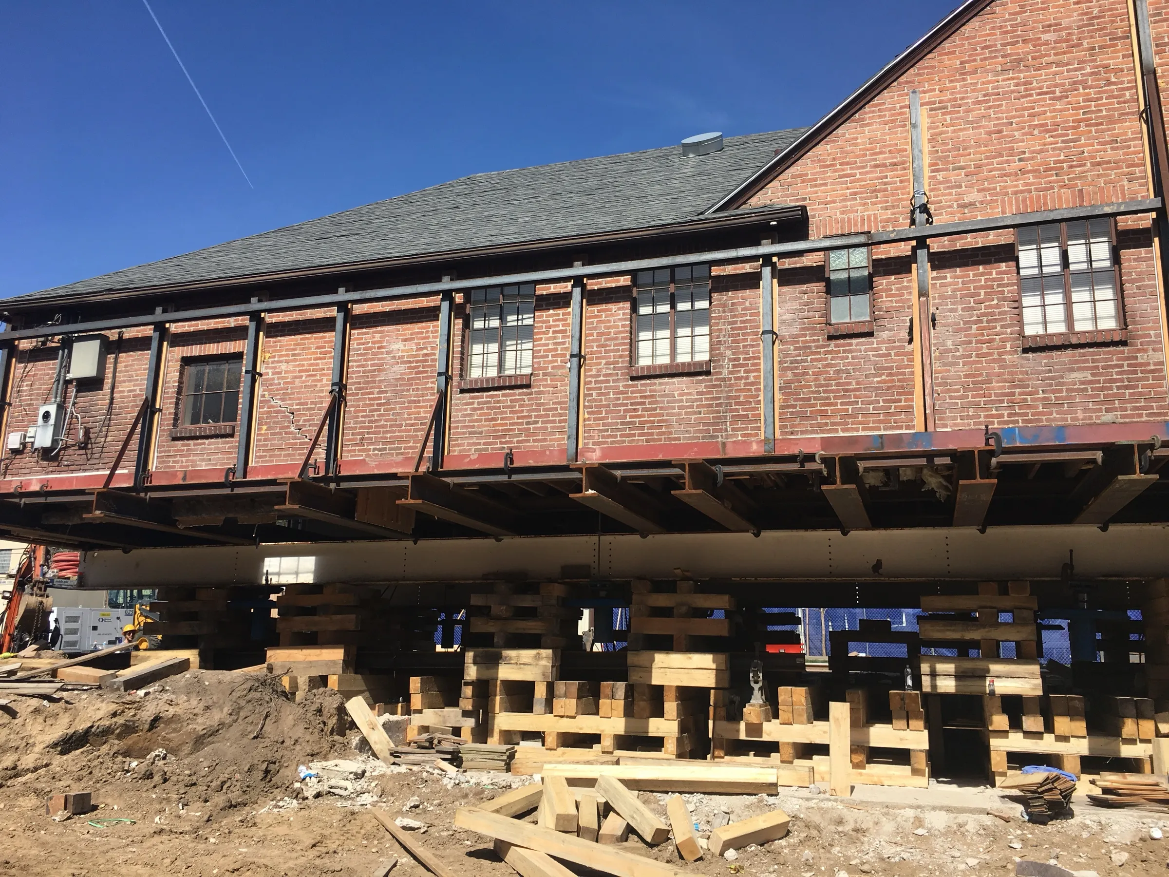 Brick building lifted onto steel beams and cribbing over its old foundation