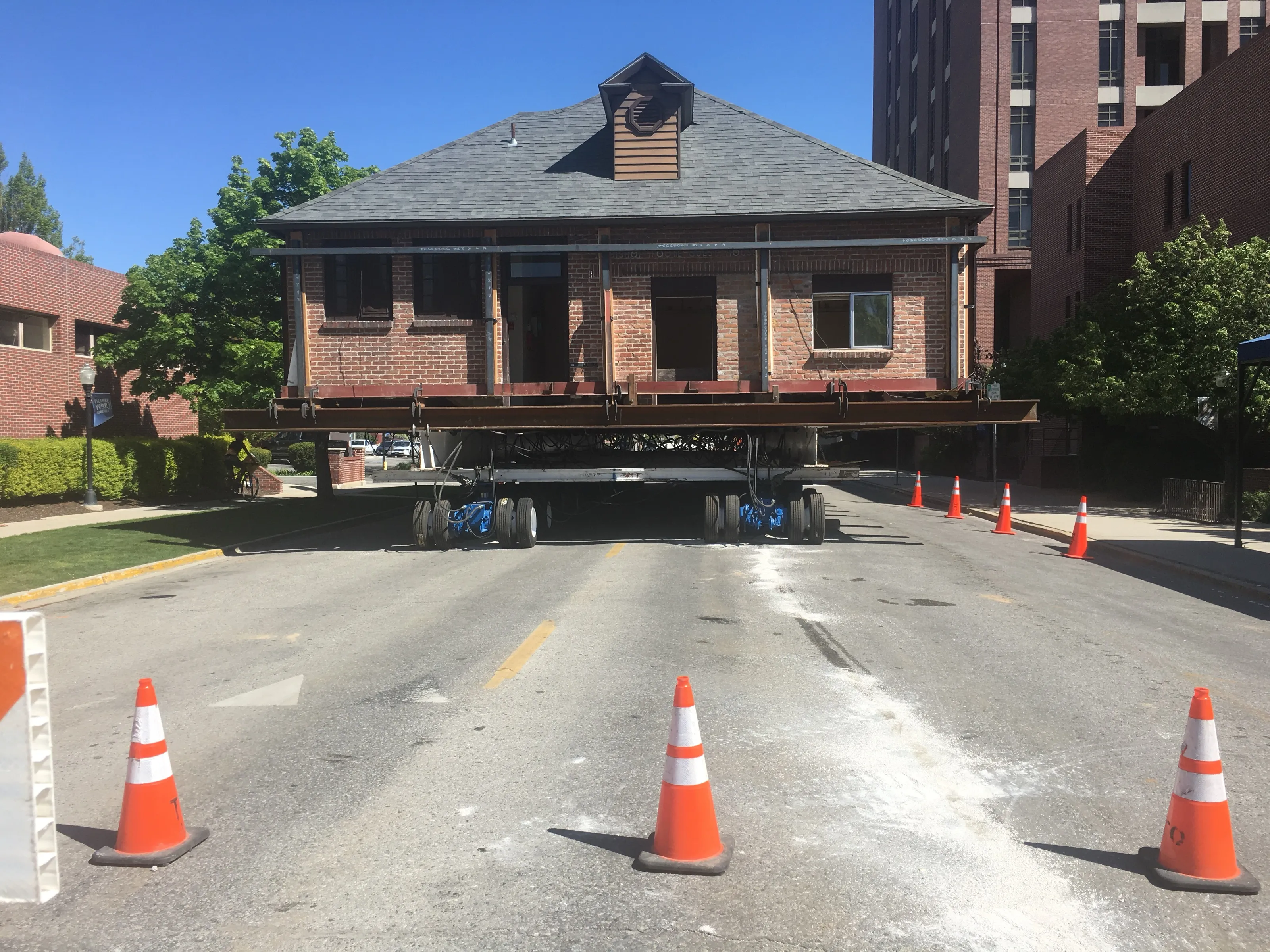 A brick building riding hydraulic dollies up a coned-off city street